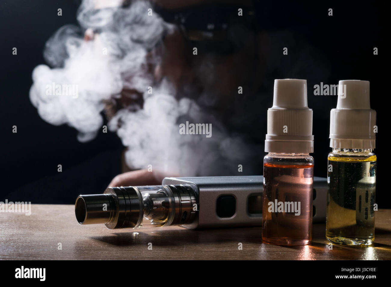 isolated e liquid and vaping device for electronic cigarette with a man vaping as a background. Stock Photo