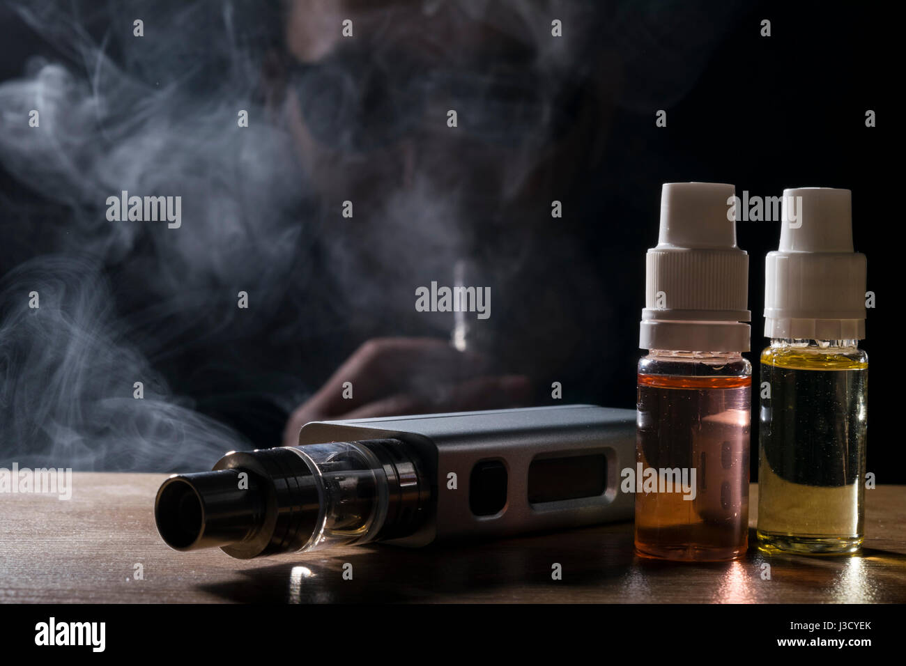 isolated e liquid and vaping device for electronic cigarette over a man on a dark background. Stock Photo