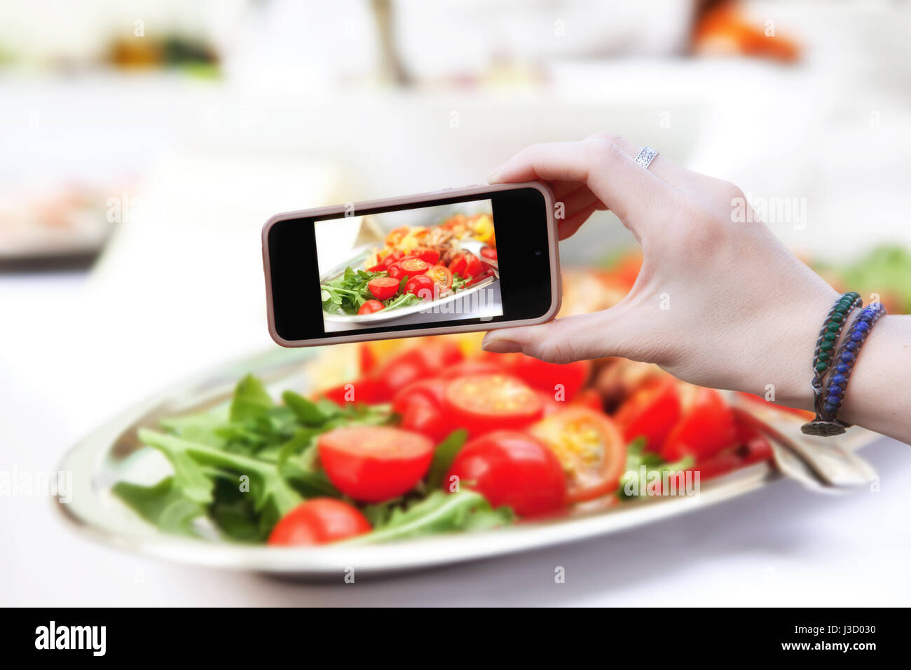 Woman holding a phone and photographed salad of red tomato Stock Photo