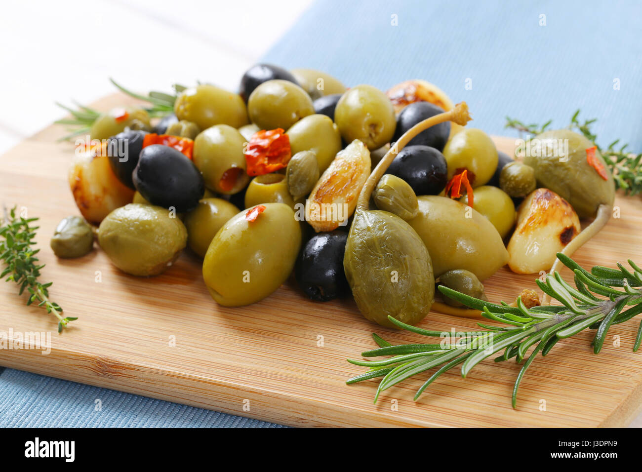 pile of pickled olives, capers, caper berries and garlic on wooden cutting board Stock Photo