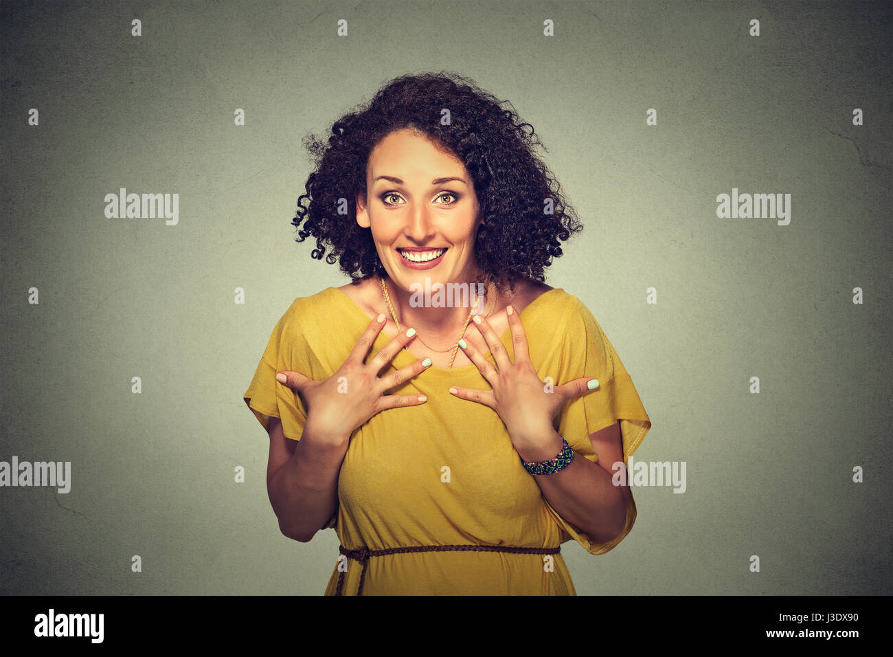 Closeup portrait of happy cute young woman looking excited, surprised in full disbelief, hands on chest, it's me? isolated on gray background. Positiv Stock Photo