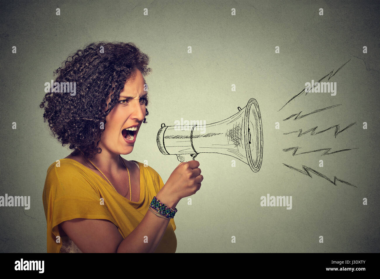 Portrait angry screaming young woman holding megaphone isolated on grey wall background. Negative face expression emotion feelings. Propaganda, breaki Stock Photo