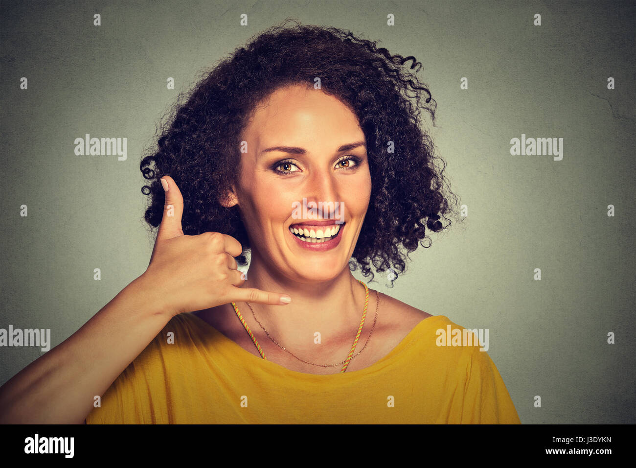Portrait attractive young woman making a call me sign and smiling isolated on gray wall background Stock Photo