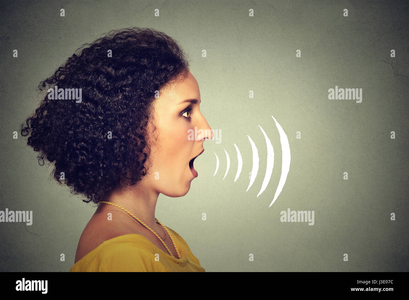 Side profile young woman talking with sound waves coming out of her mouth isolated on grey wall background. Human face expressions Stock Photo