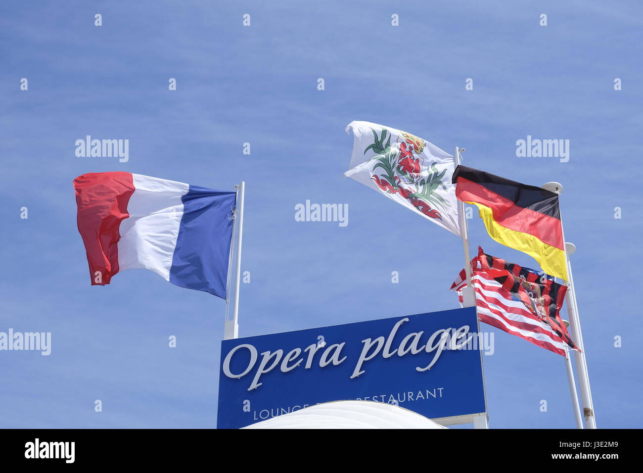 Nice, Provence-Alpes-Côte d'Azur, France. French, German and Nice flags flying over the Opera Plage (beach) Stock Photo