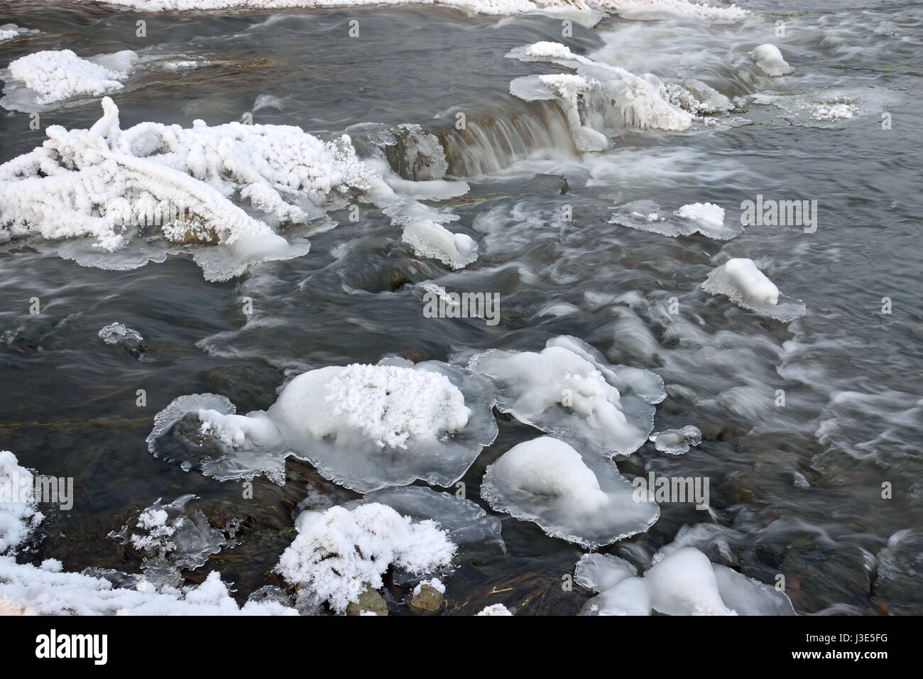 Foaming rapids of the river, covered with growths of ice and bushes dry grass in hoarfrost crystals on the shores of a winter evening Stock Photo