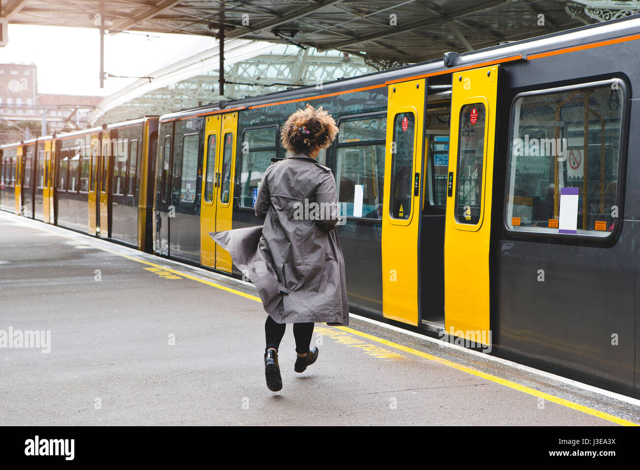 Rear view of a woman running to catch the train before it leaves the station without her. Stock Photo