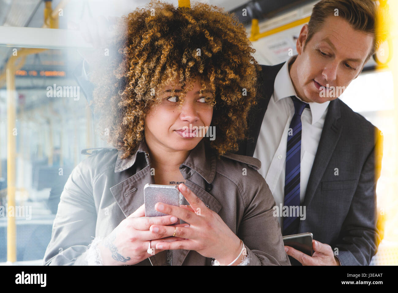 Man looking over a womans shoulder on the train at her phone screen. Stock Photo