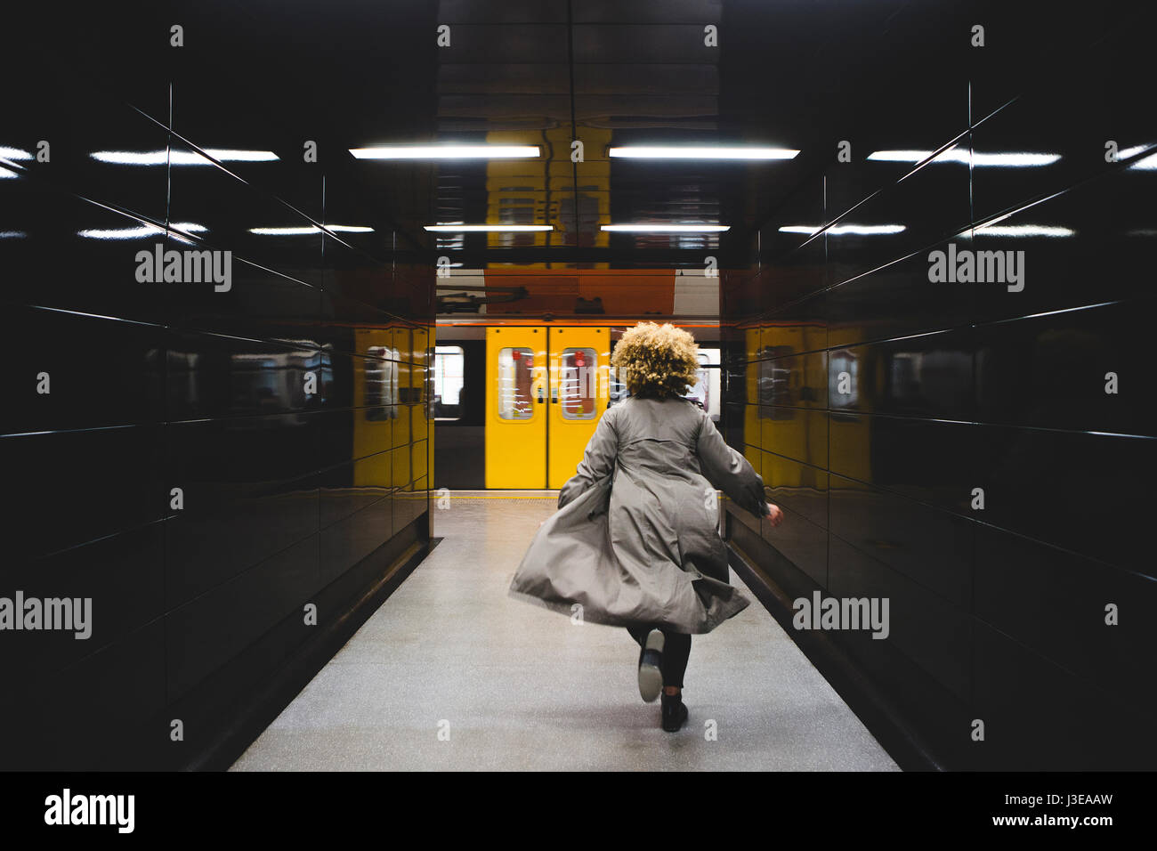Rear view of businesswoman running to catch the subway train, which is already leaving the underground station. Stock Photo