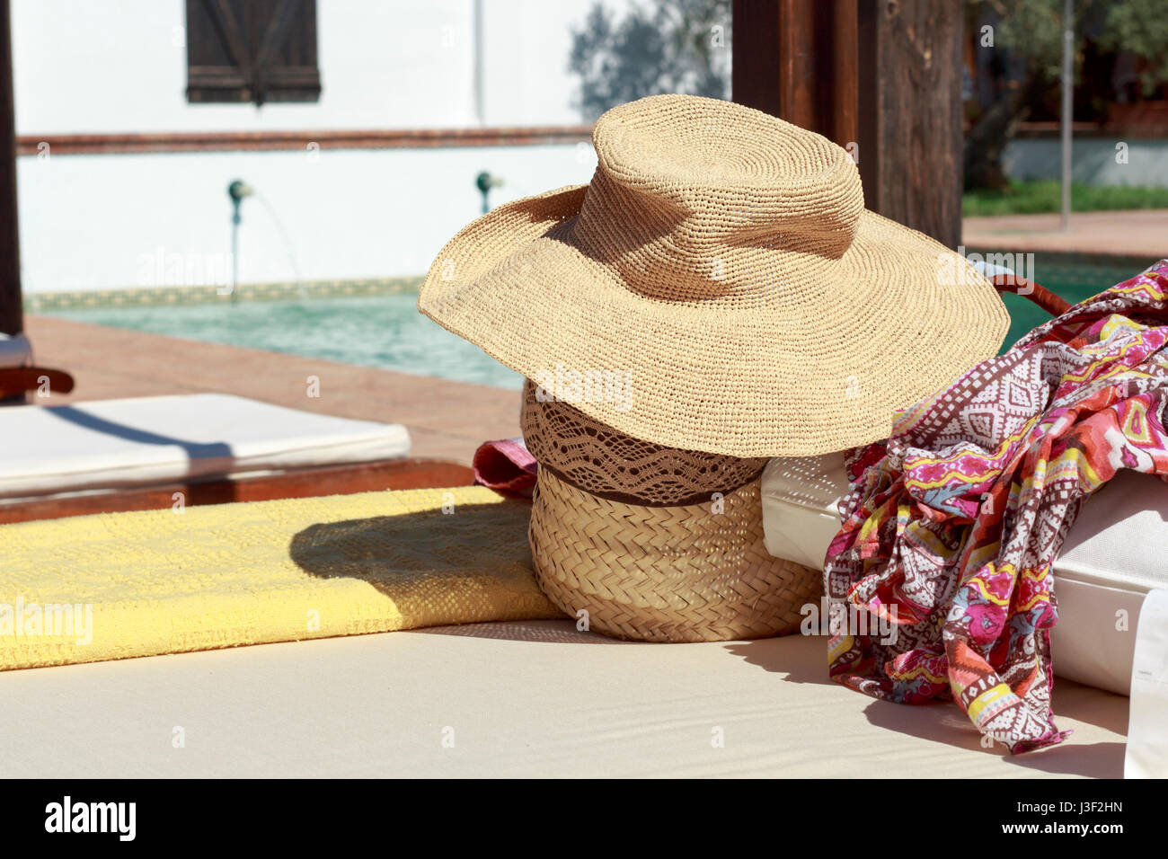Sun hat, beach bag and pareo on deck chair beside a swimming pool Stock Photo