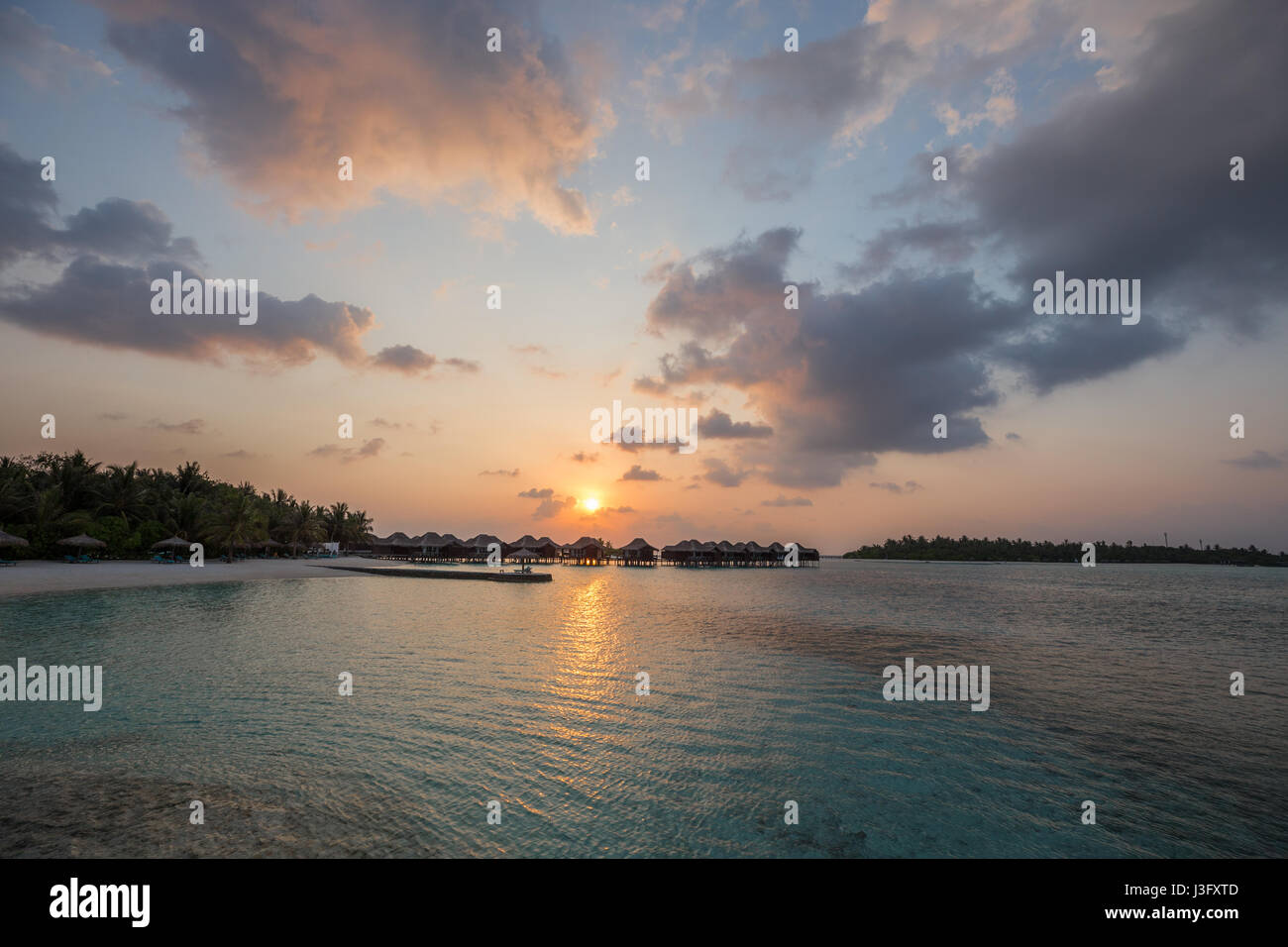 Tropical Paradise Sunset Sunrise View of Over Water Bungalows with Orange Red Sky Stock Photo