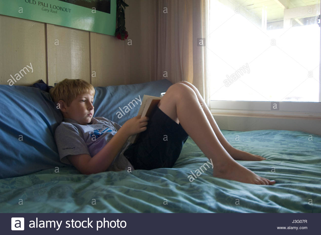 Boy Lying On Bed With Head On Pillow Reading A Book Stock Photo
