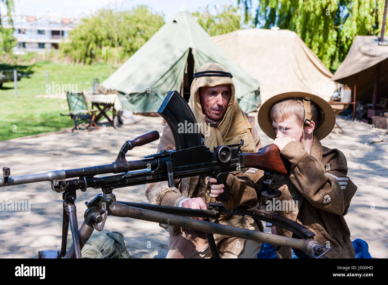 Salute to the 40s re-enactment. Child, blonde boy, 6-7 years old, in British army uniform, being shown how to fire Bren gun by Desert Rat soldier. Stock Photo