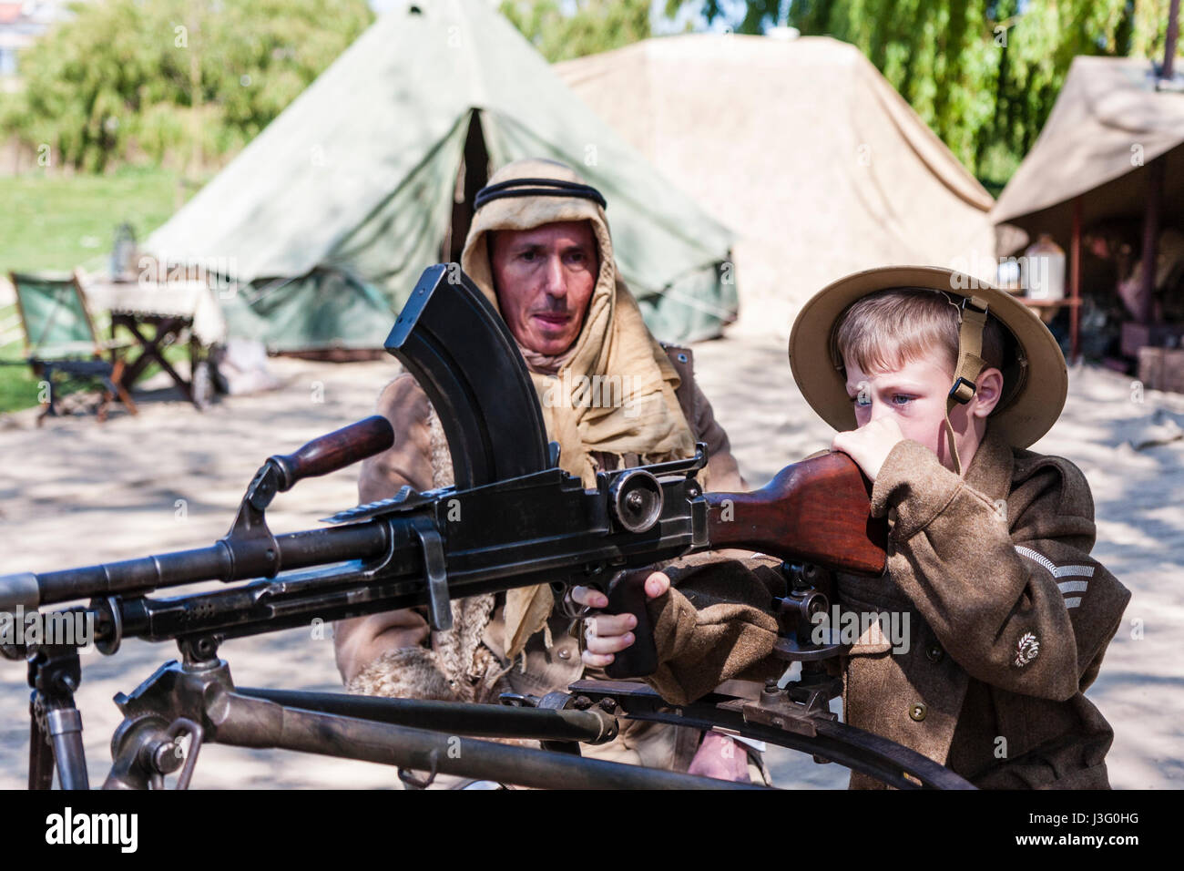 Salute to the 40s re-enactment. Child, blonde boy, 6-7 years old, in British army uniform, being shown how to fire Bren gun by Desert Rat soldier. Stock Photo