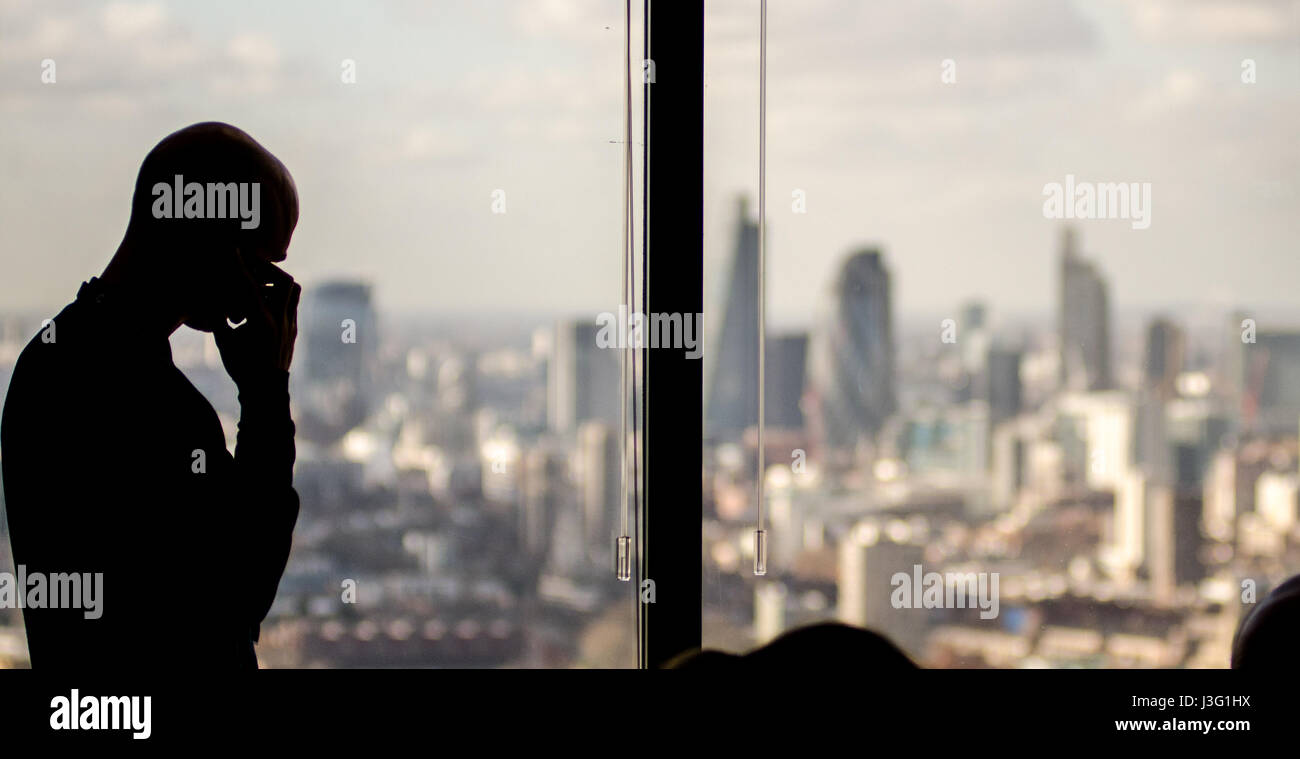 London, England, UK - February 27, 2015: A businessman making a call on a mobile phone is silhouetted in the window of a Docklands office skyscraper,  Stock Photo