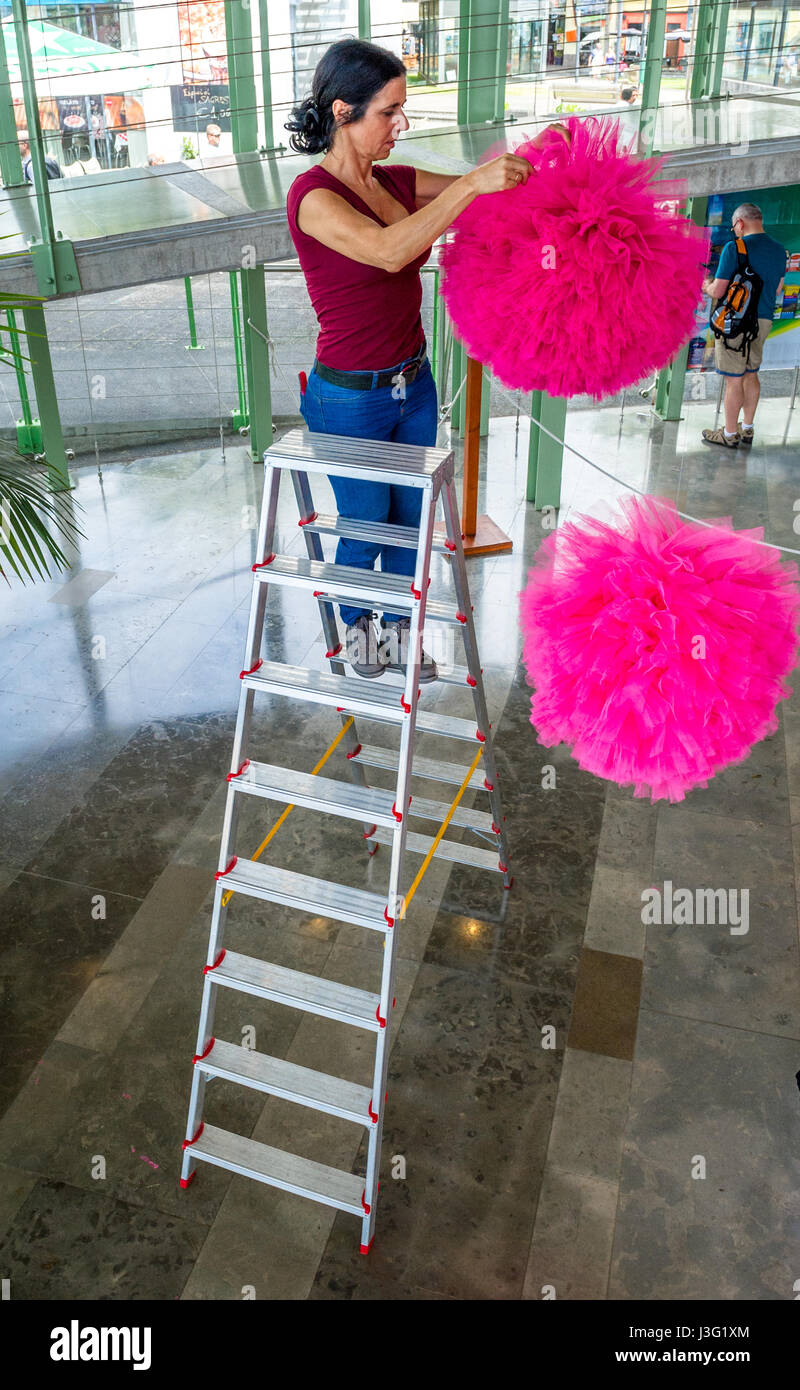 Woman hanging large pink pom poms at the cable car base station in Funchal, Madeira. Stock Photo
