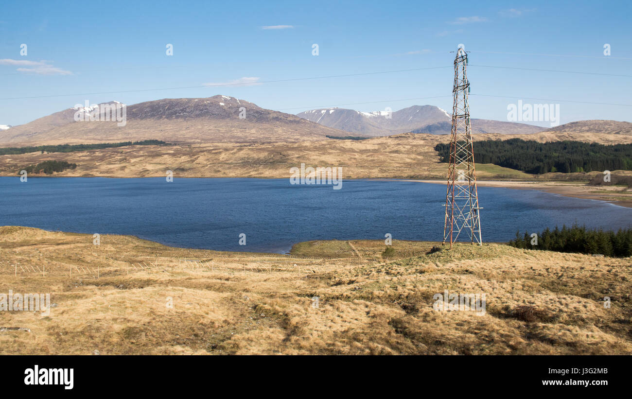 Power lines run alongside Loch Tulla and mountains near Bridge of Orchy and Rannoch Moor in the remote West Highlands of Scotland. Stock Photo