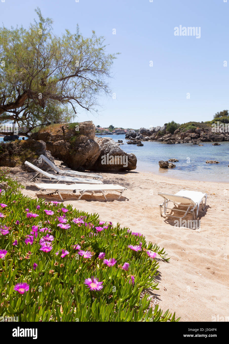 beautiful beach of Stoupa in greece on sunny day in spring on peloponnese with flowers and sunbeds and village in the background Stock Photo