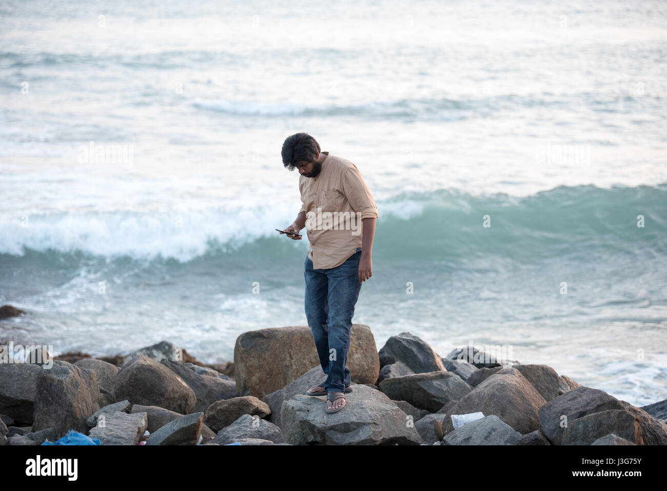 Men looking at hin smart phone an a beach in Kanyakumari, India Stock Photo