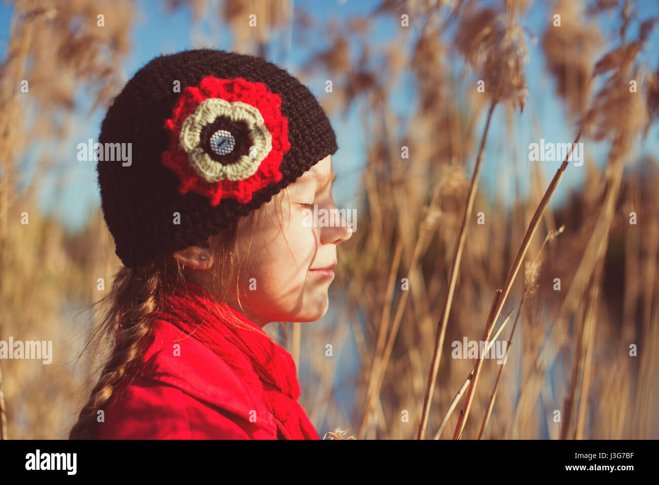 child girl closed her eyes against the sun by bright springtime day inside dry reed stalks Stock Photo