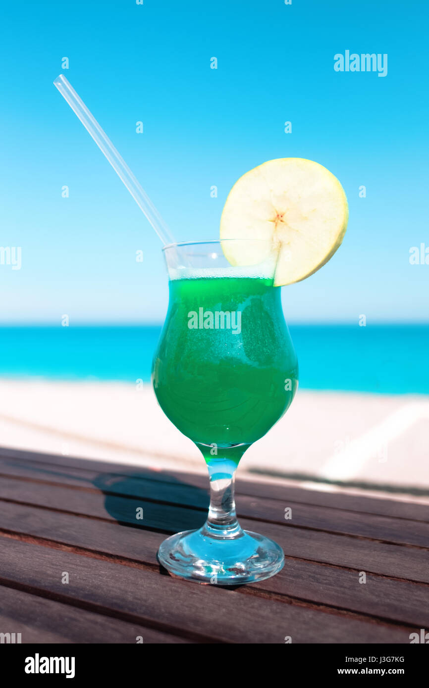 Green cocktail with apple piece on wooden table. Sunny day near mediterranean sea. Summer time Stock Photo
