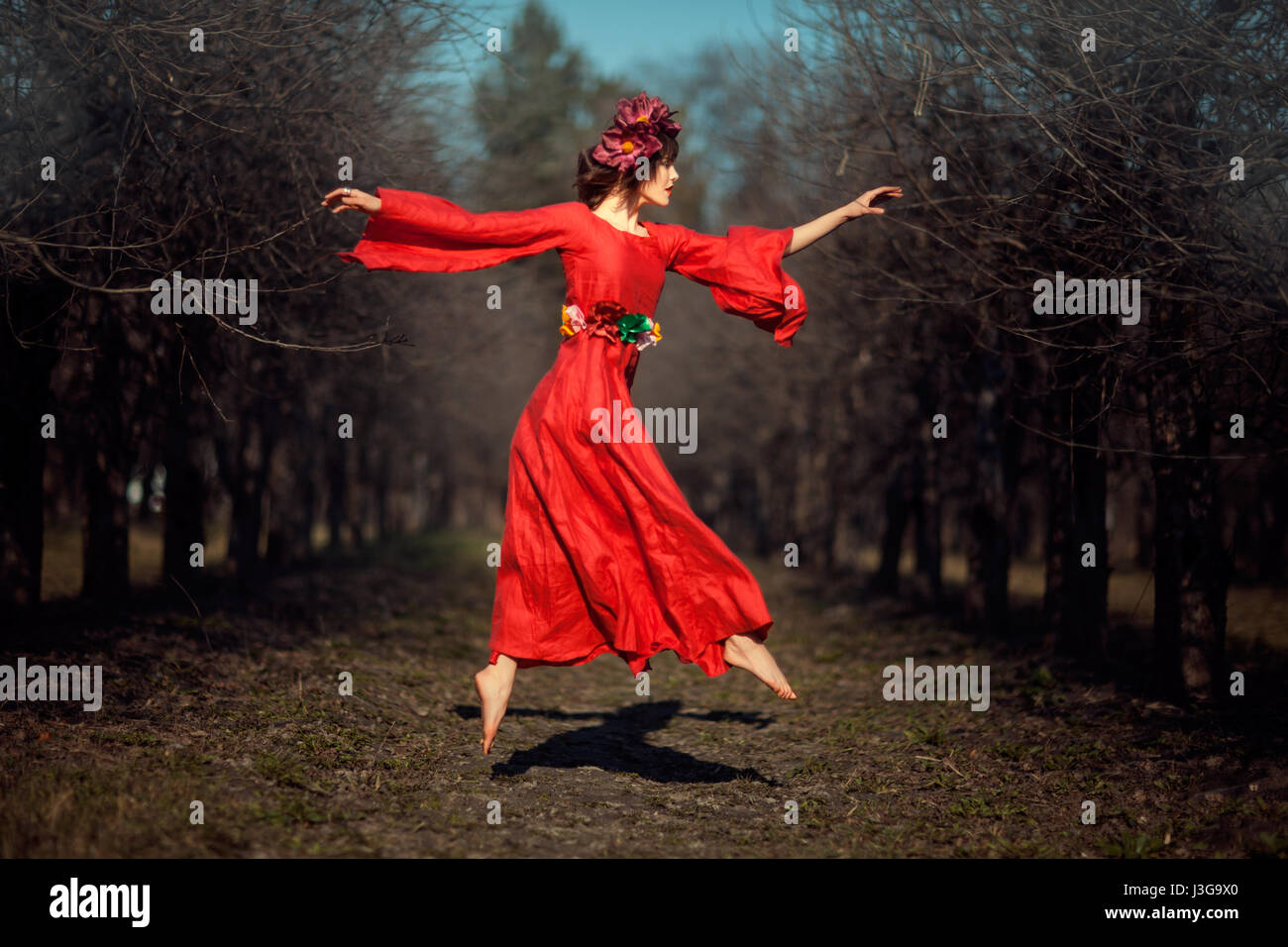 In autumn park floating girl in a red dress with a wreath on his head like a fairy tale. Stock Photo