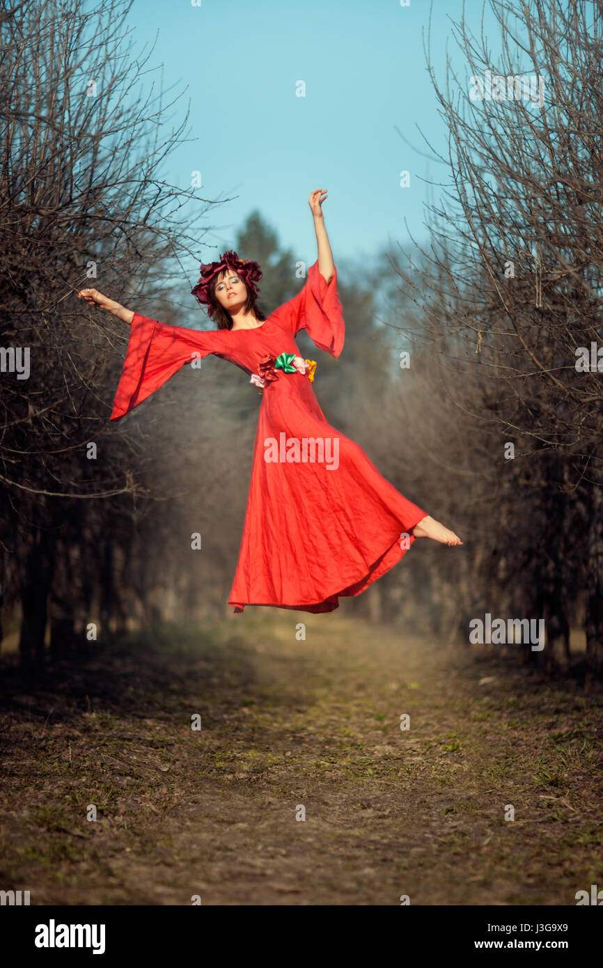 In the park among the trees levitating girl with a wreath of flowers on her head. Stock Photo