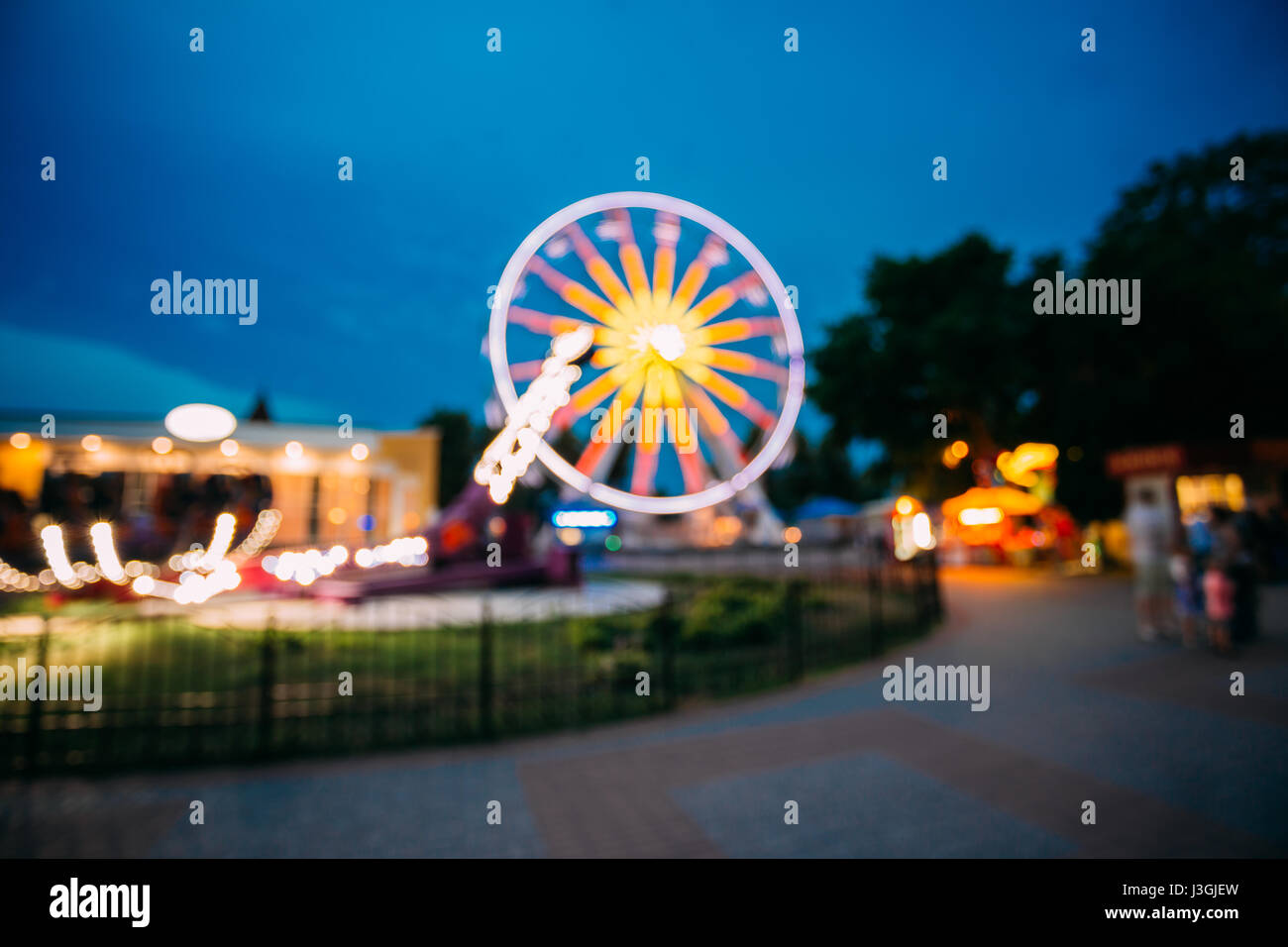 Abstract Motion Blur Image Of Brightly Colorful Illuminated Ferris Wheel In Amusement City Park On Black Blue Evening Sky Bokeh Boke Background. Stock Photo