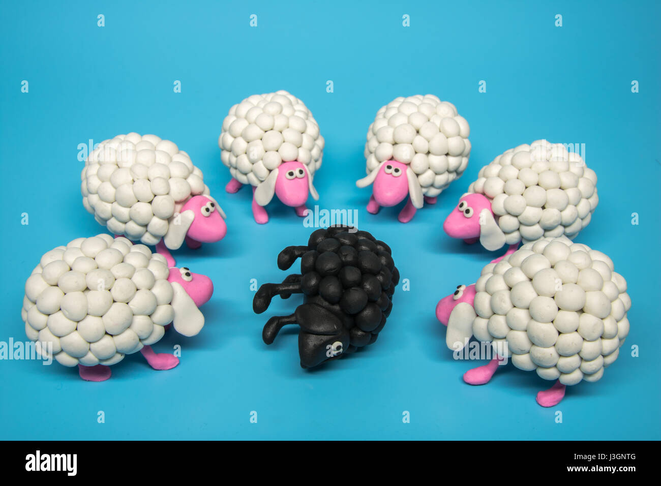 Concept - A group of white polymer clay sheep surrounding a black sheep lying on its side Stock Photo