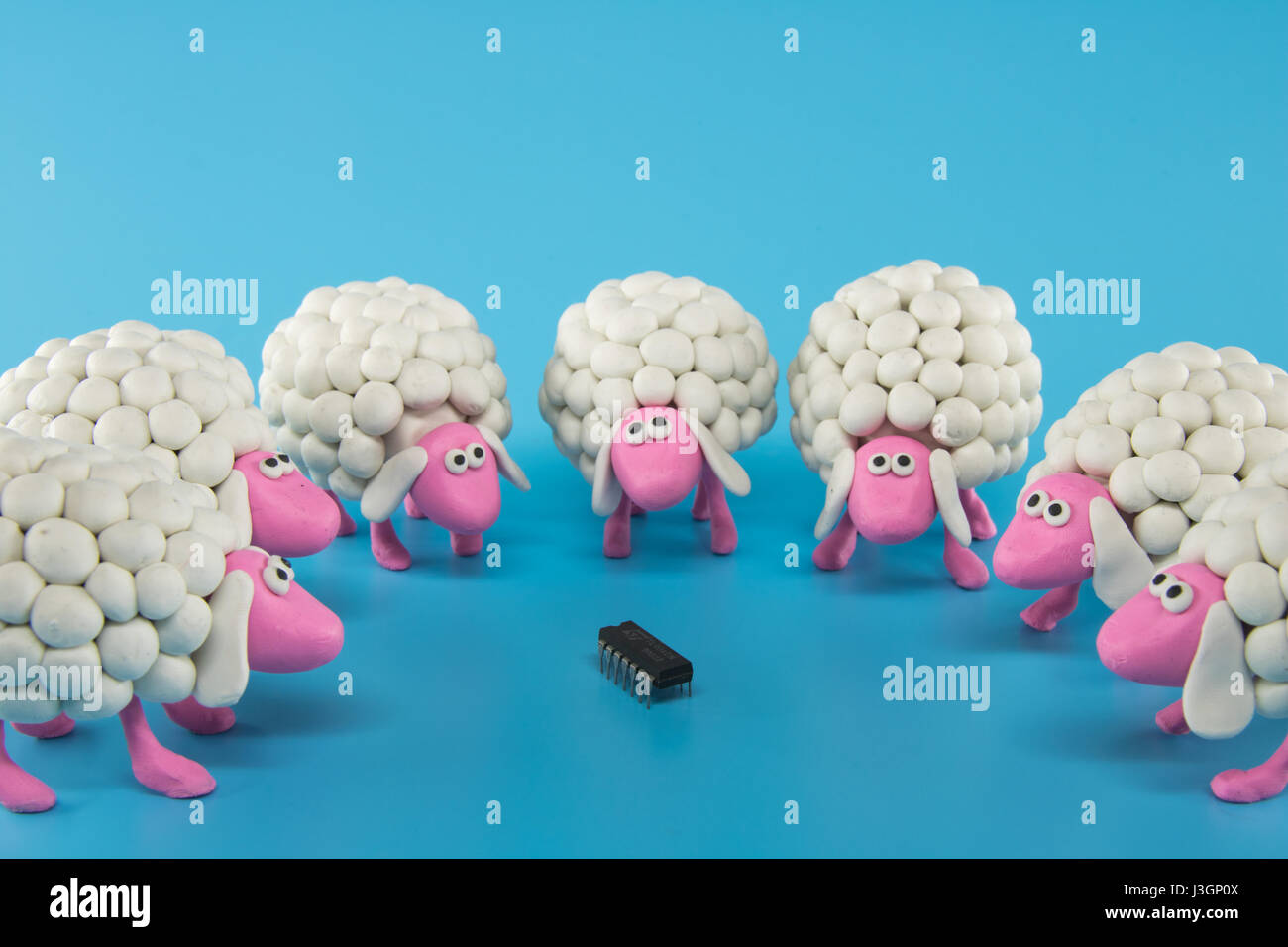 White polymer clay sheep gather around an electronic chip on a blue background Stock Photo