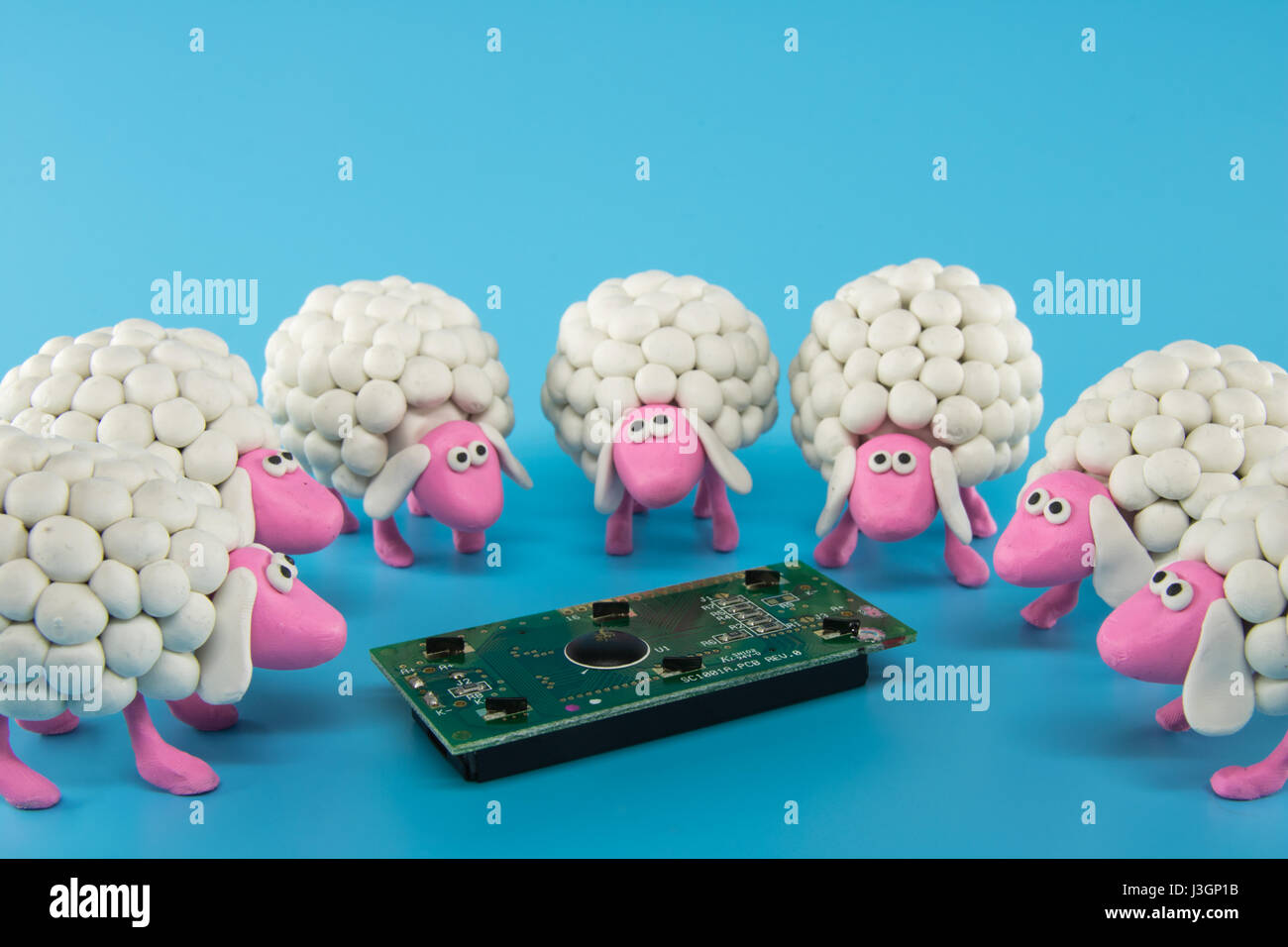 White polymer clay sheep gather around an electronic circuit on a blue background Stock Photo