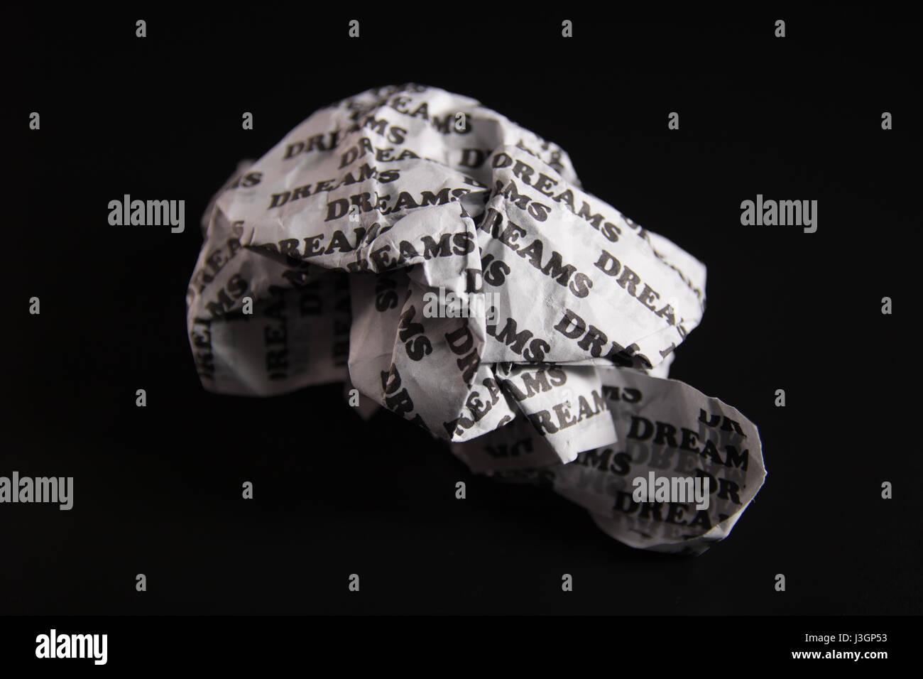 A crumpled paper with the words 'dreams' written all over it on a black background. Stock Photo