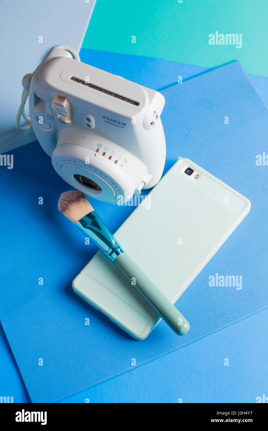 Her life on blue shades: Still Life of an instant camera, smartphone and a make-up brush placed in a multi colored blue shades Stock Photo