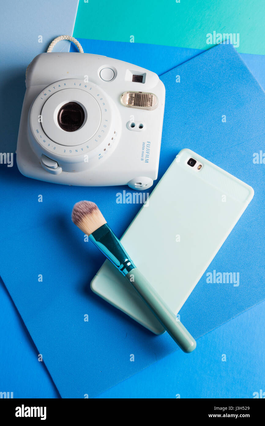 Her life on blue shades: Still Life of an instant camera, smartphone and a make-up brush placed in a multi colored blue shades Stock Photo