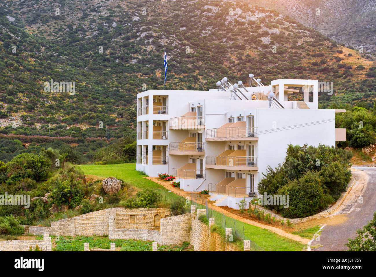 Modern Greek architecture, new white building in constructivist style, stands on shore of Cretan sea. On flagpole flag of Greece. Resort village Bali, Stock Photo