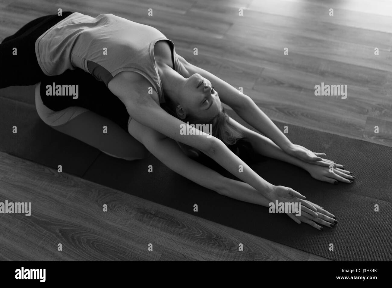 Black-white photo of young sportswomen in gym doing yoga Stock Photo