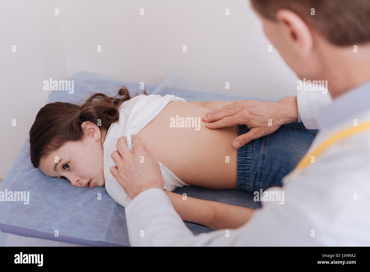 Does it hurt. Professional capable gentle rheumatologist examining the spine of the child while she experiencing pain and needing professional treatme Stock Photo
