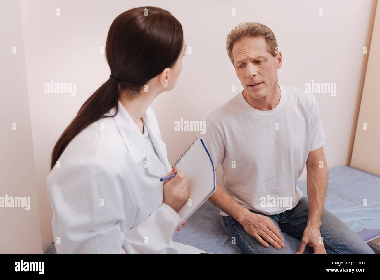 Pain is unbearable. Concerned hurt middle aged patient visiting his doctor and explaining what he feeling while having some troubles with his back Stock Photo