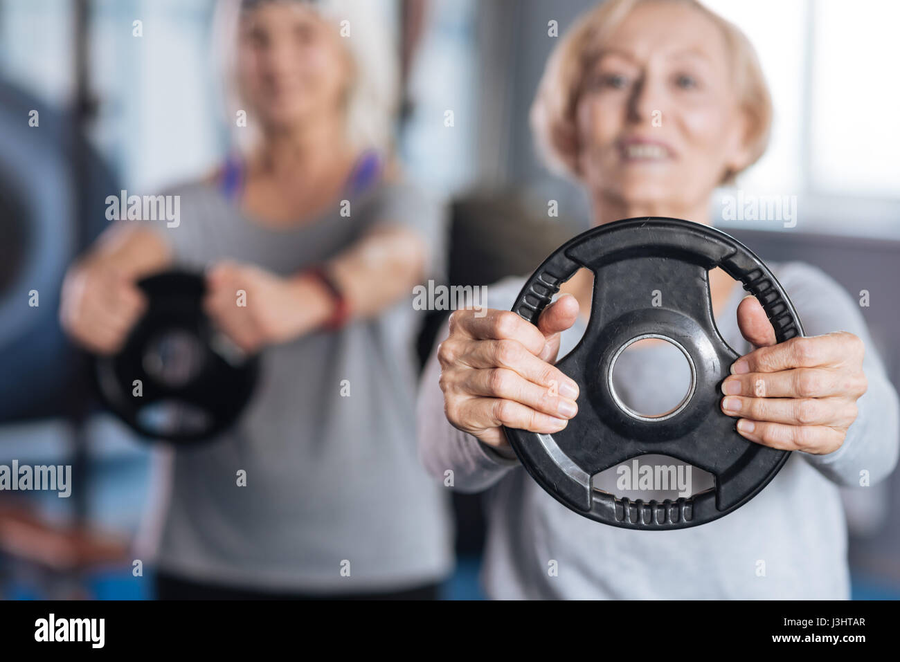 Physical activities. Selective focus of a weight disc being held by a nice active aged woman while doing physical activities Stock Photo