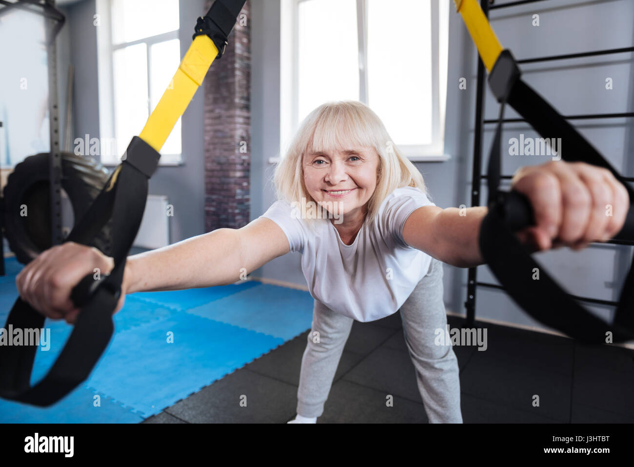 Doing exercises. Happy positive aged woman bending forward and exercising while using sports equipment Stock Photo