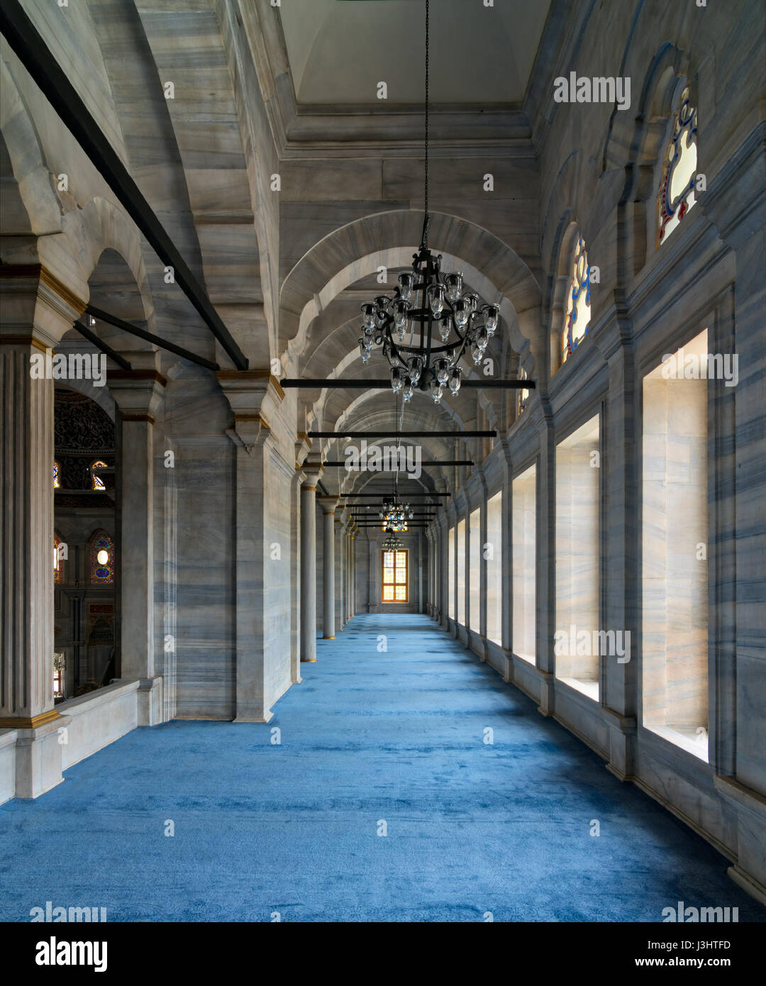 Passage in Nuruosmaniye Mosque, a public Ottoman Baroque style mosque, with columns, arches and floor covered with blue carpet lighted by side windows Stock Photo