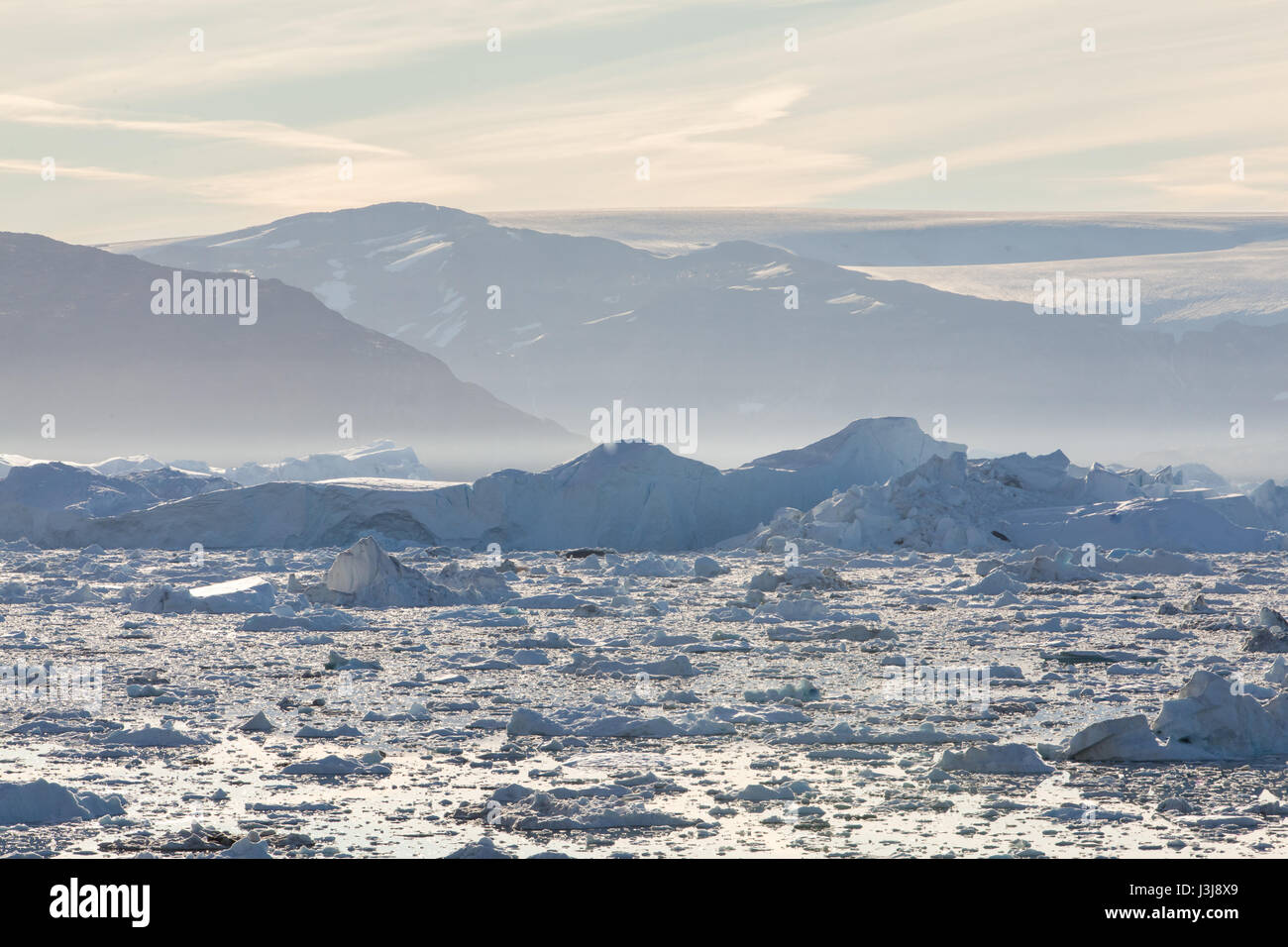 A bay filled with icebergs and bergy bits with mountains and glaciers ...