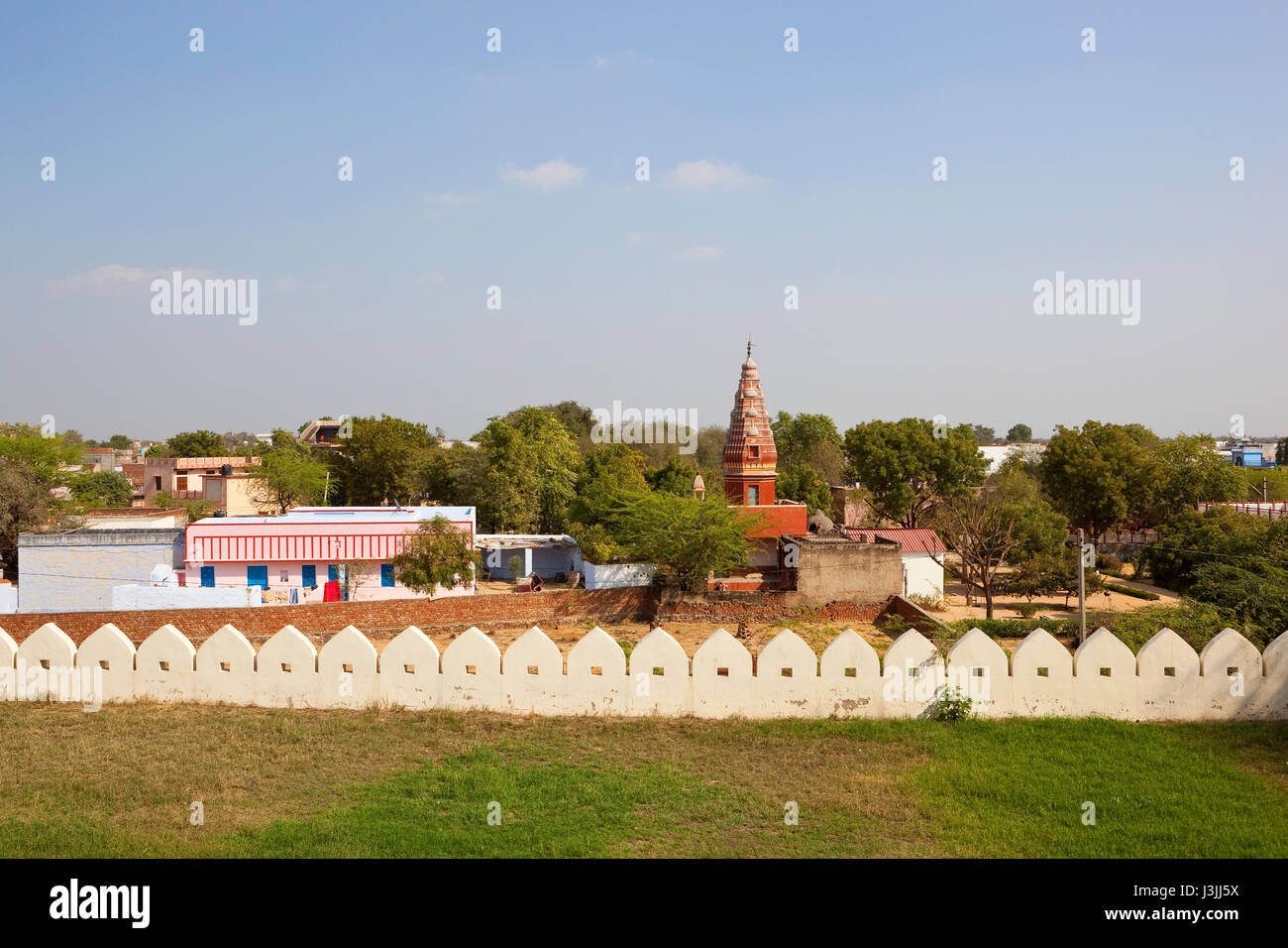 a small hindu temple in the town of Surajgarh surrounded by houses and trees under a blue cloudy sky Stock Photo