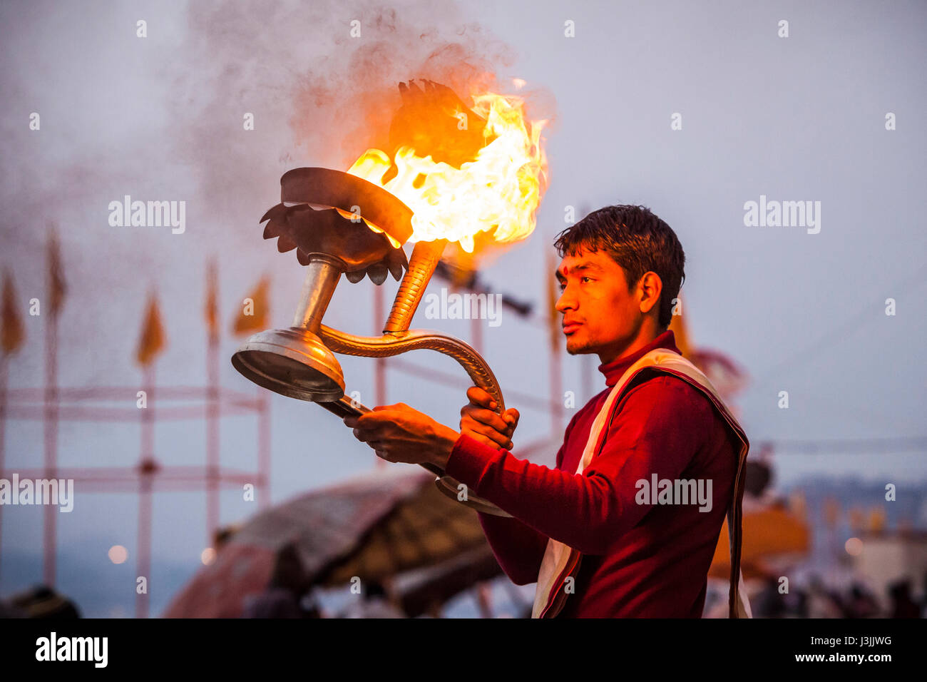 A Hindu priest on the shores of the Ganges / Ganga river in Varanasi, India performs a ceremony (puja) with an oil lamp. Stock Photo