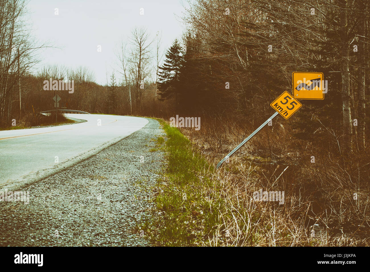 Bent over speed limit sign beside rural road. Grunge look applied. Stock Photo