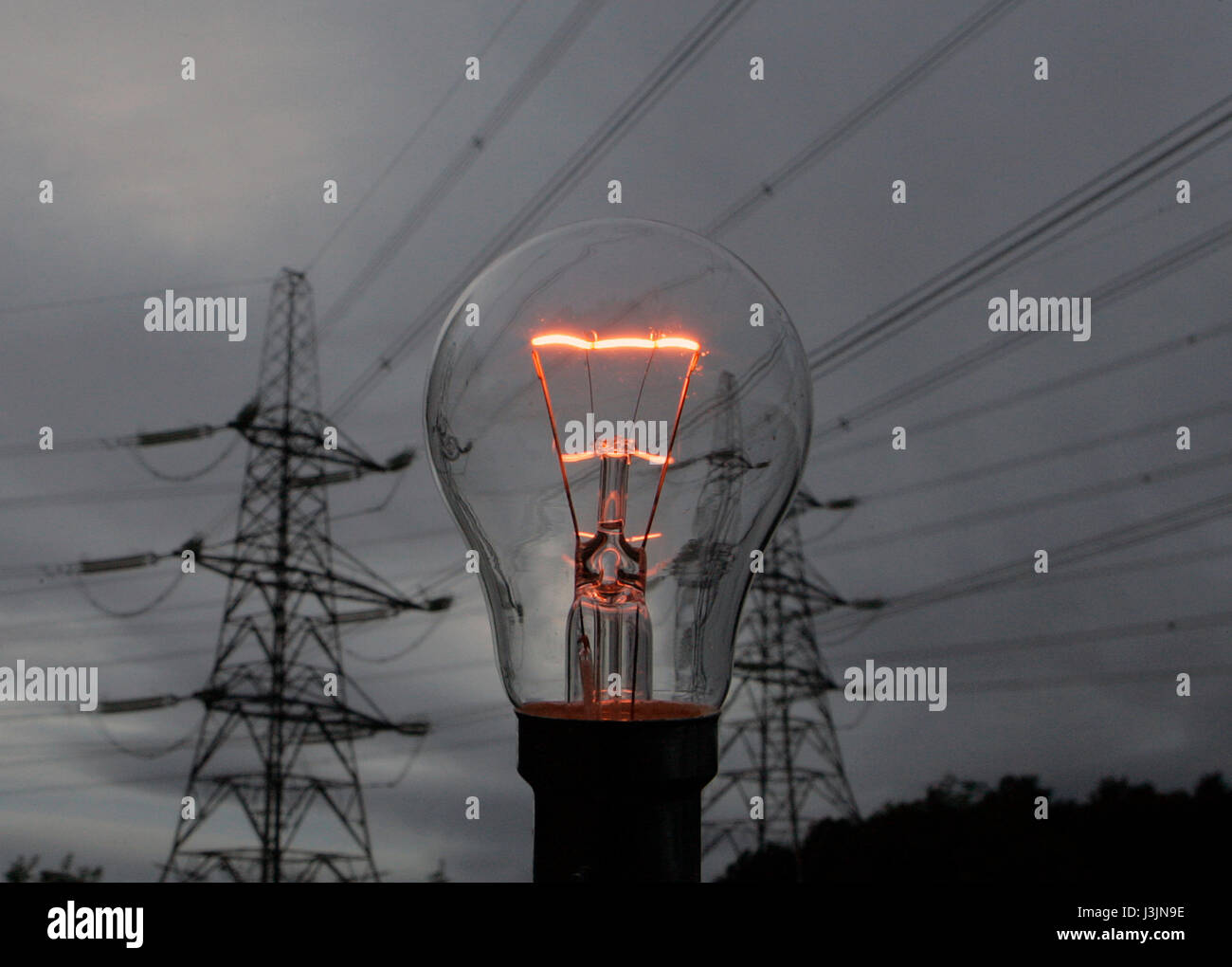 High voltage electricity grid  power supply lines at dusk with an illuminated  filament in an incandescent light bulb in Central Scotland Stock Photo