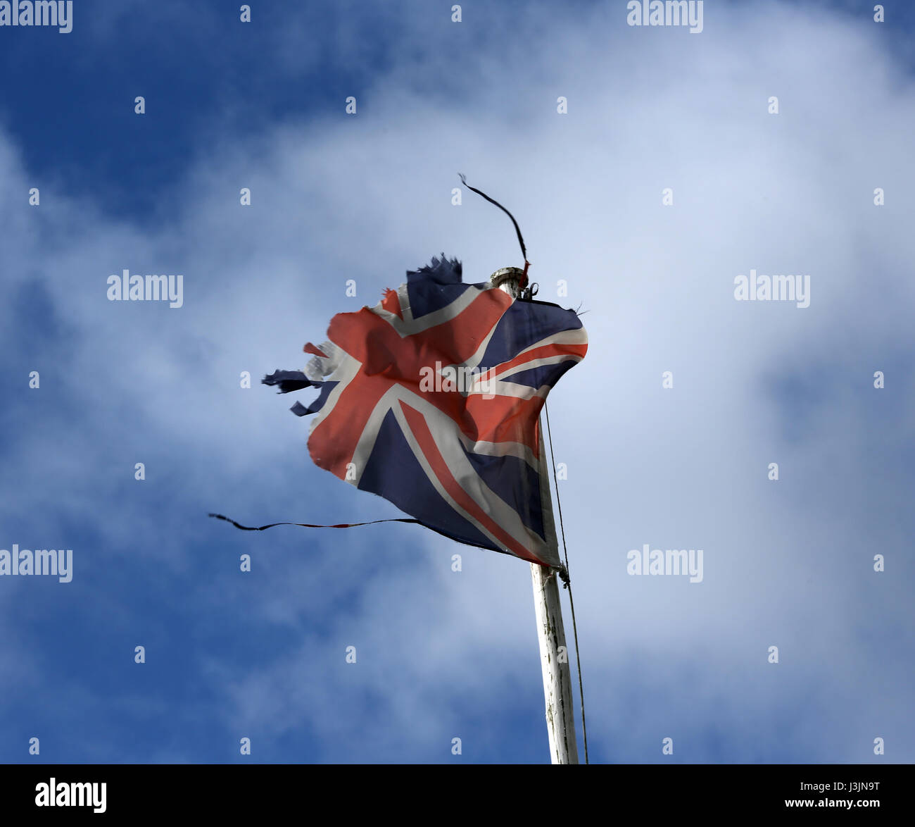 A tattered Union Flag blowing in the wind pictured against a cloudy bright blue sky of a flagpole in Ballater Scotland Stock Photo