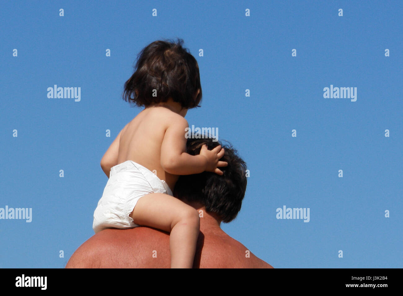 Little girl riding on her fathers shoulders in the blue sky Stock Photo