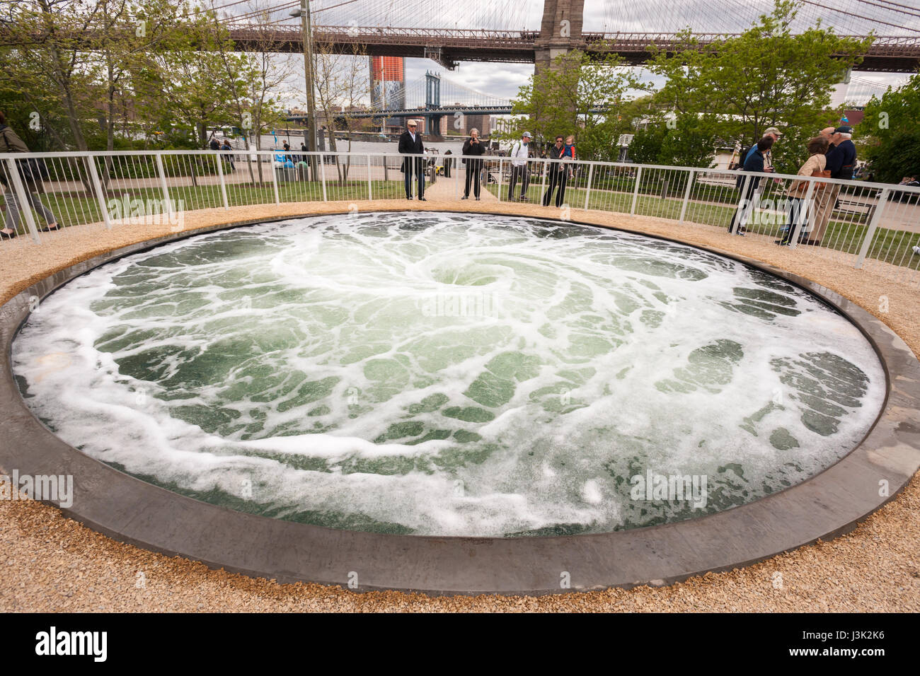 Visitors to Brooklyn Bridge Park in New York on Wednesday, May 3, 2017 are enthralled by the artist Anish Kapoor's 'Descension' installation. The artwork consists of a continuously swirling vortex of water in a 26 foot wide pool hypnotically commanding the attention of the viewer as it is reminiscent of being sucked into the depths. The installation is funded by the Public Art fund which is celebrating its 40th anniversary. 'Descension' will be on view until September 10, 2017 on Pier 1 in the park. (© Richard B. Levine) Stock Photo