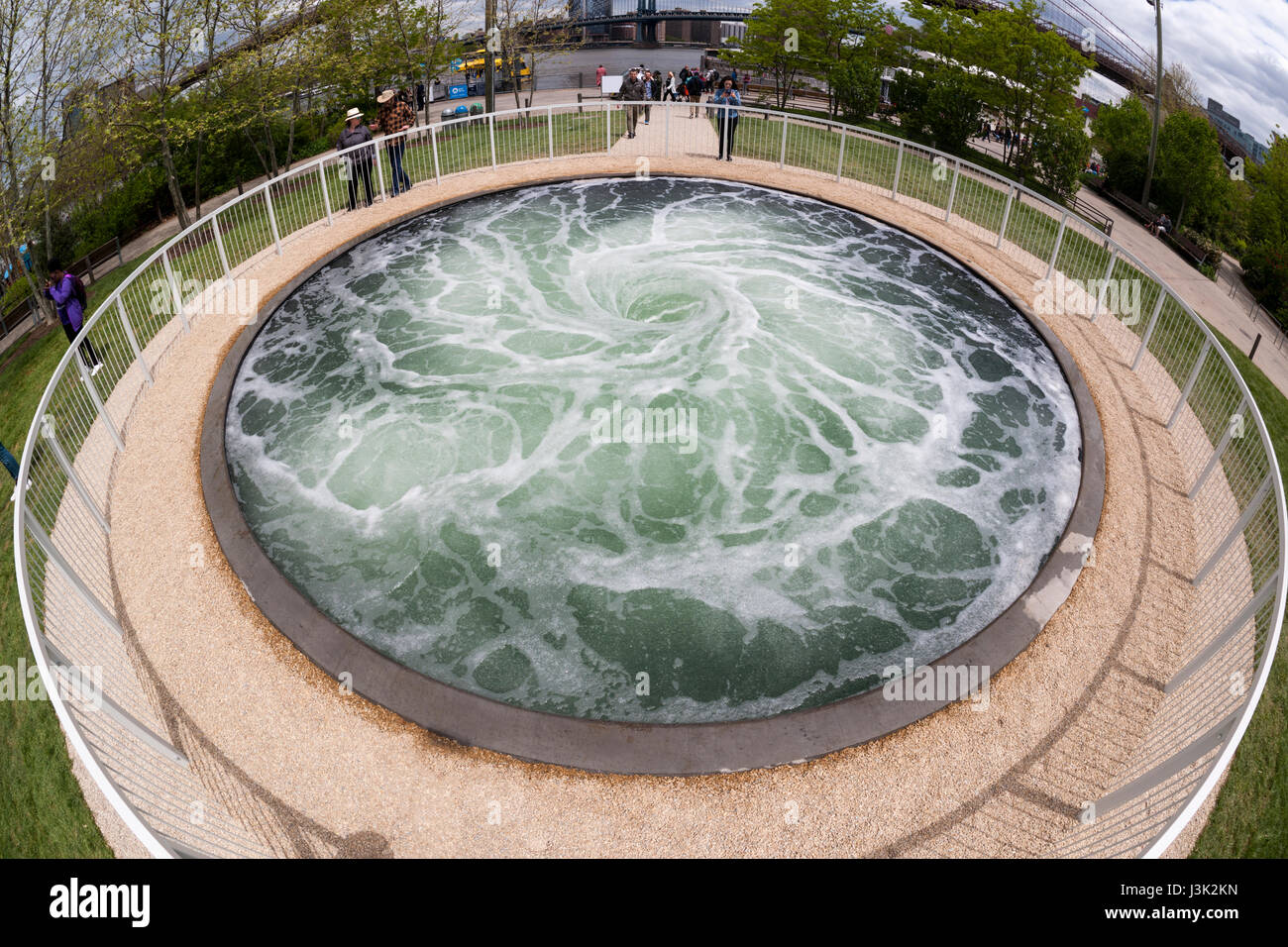 Visitors to Brooklyn Bridge Park in New York on Wednesday, May 3, 2017 are enthralled by the artist Anish Kapoor's 'Descension' installation. The artwork consists of a continuously swirling vortex of water in a 26 foot wide pool hypnotically commanding the attention of the viewer as it is reminiscent of being sucked into the depths. The installation is funded by the Public Art fund which is celebrating its 40th anniversary. 'Descension' will be on view until September 10, 2017 on Pier 1 in the park. (© Richard B. Levine) Stock Photo